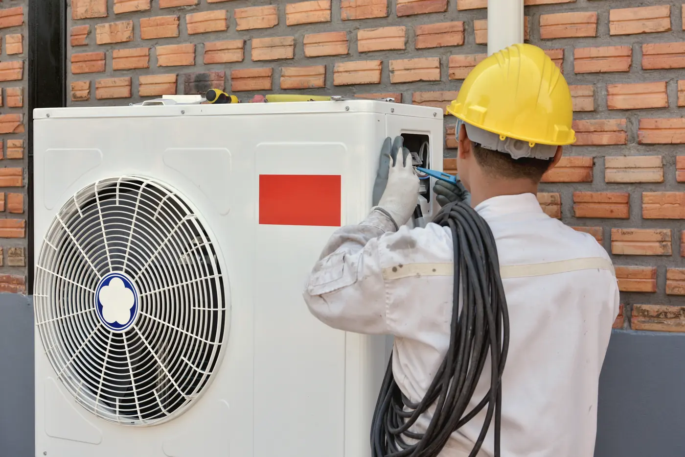Technicien installant l'unité extérieure d'une thermopompe sur un mur de brique