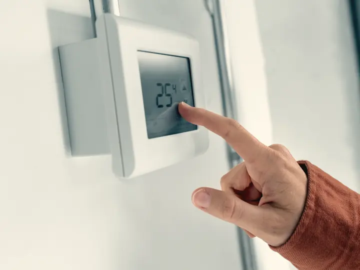 Doigt réglant un thermostat intelligent au mur