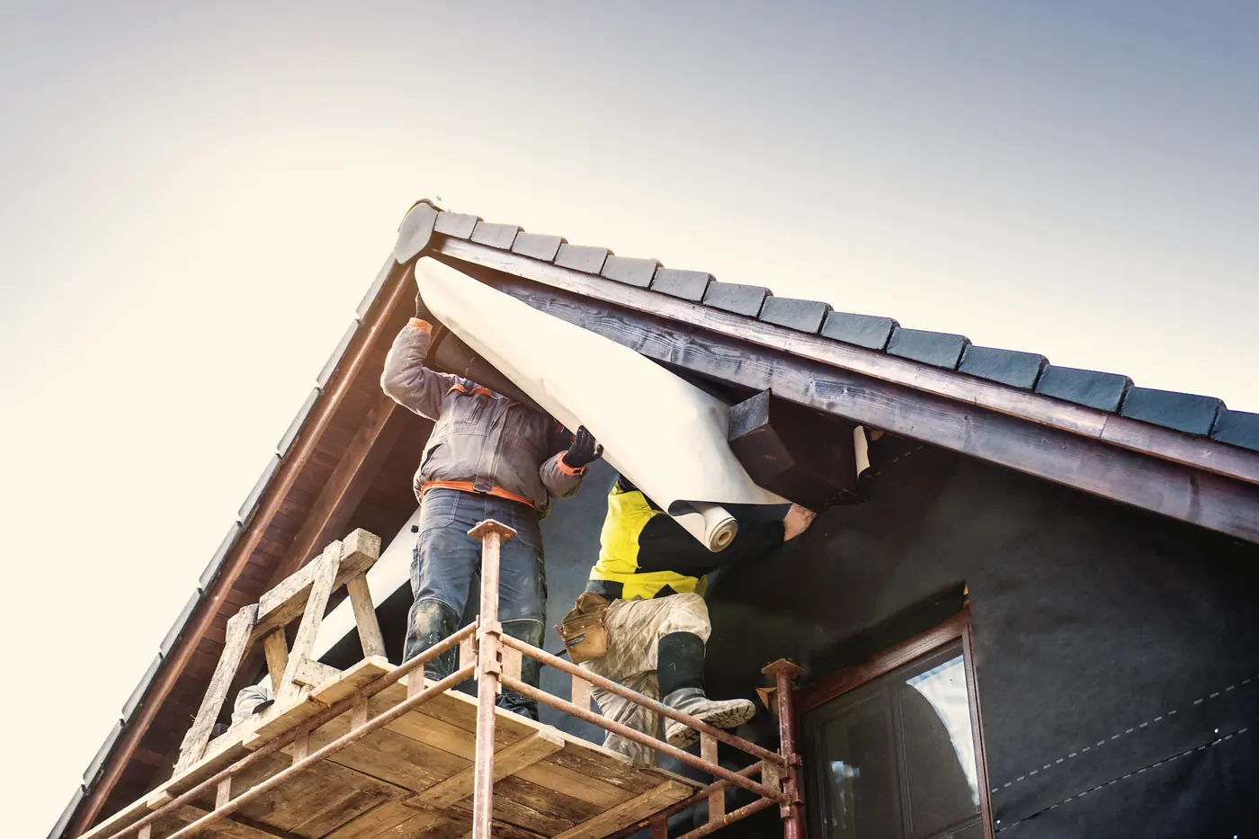 Ouvriers refaisant la toiture d'une maison depuis un échafaud